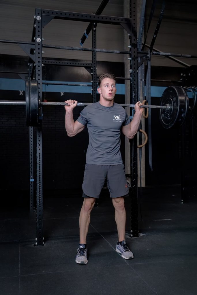 Man doet squats met zware halter in sportschool.