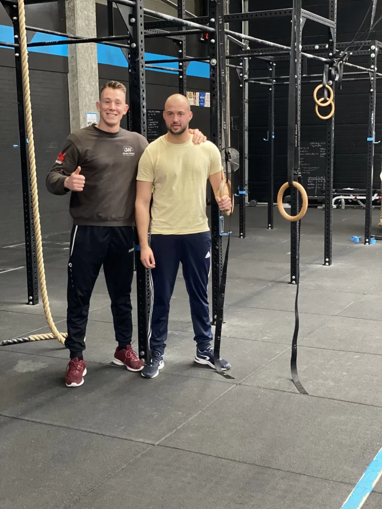 Twee mannen in sportschool met ringen en touwen.