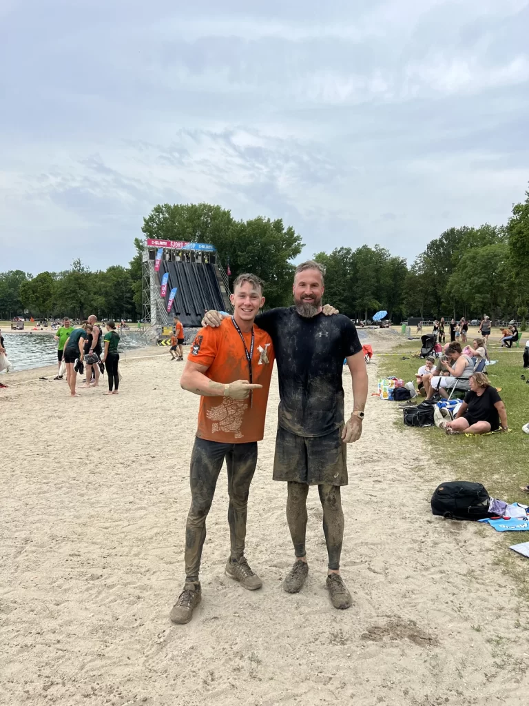 Twee mannen na modderrace op strand.